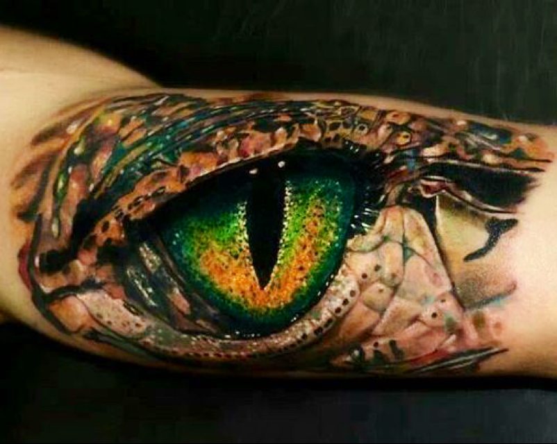 Primer plano de tatuador profesional realizando un tatuaje a color detallado de fénix y flores en el antebrazo